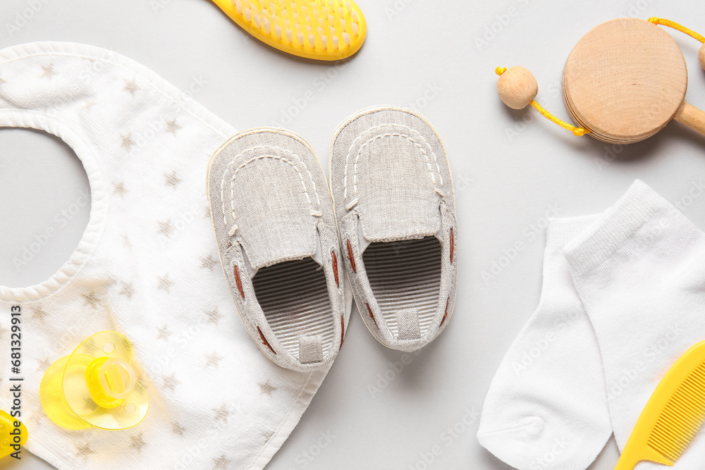 Stylish baby shoes with bib, socks, brushes and pacifier on grey background