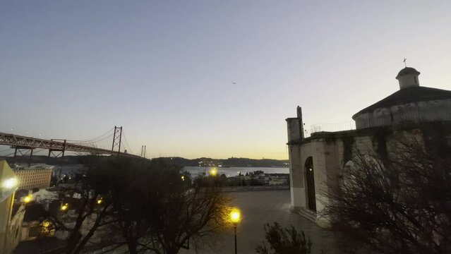 Santo Amaro Chapel in Lisbon, Portugal, Europe, with plane coming in to land at sunset at end of Autumn, beginning of winter. 25th April Bridge in background