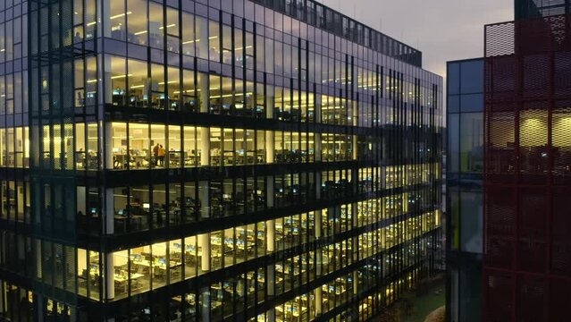 Aerial view of a modern office building at night. Cinematic shot of a drone on Windows office building and working people. Modern office building with big windows at night, in windows light shines 