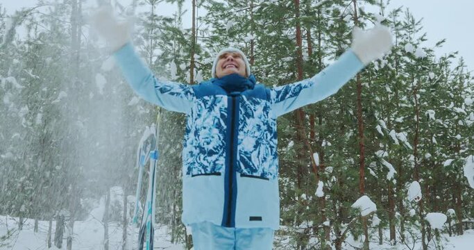 A happy woman throws snow into the sky and jumps, rejoices at the beginning of winter and a winter walk through the forest. Maintaining the psychological health of the elderly. High quality 4k footage