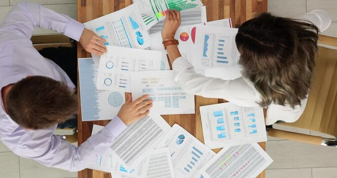 Two business professionals nervously analyzing business documents, top view