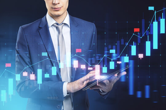 Attractive young european businessman with pad using glowing blue candlestick forex chart on blurry background. Financial growth, stock and exchange concept. Double exposure.