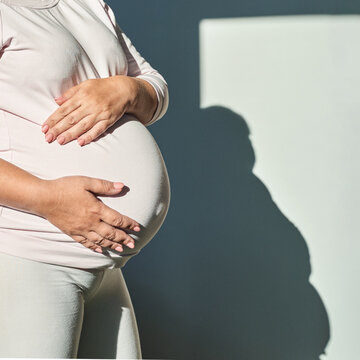 怀孕的白人女性在阳光照耀的房间里抚摸着肚子，尽显母性与期待。