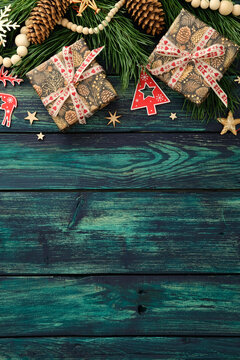 质朴青绿色木板上摆放着两个包装好的礼物、松枝、松果、红色驯鹿和树木剪纸的节日平面布置图，温馨的圣诞背景设计