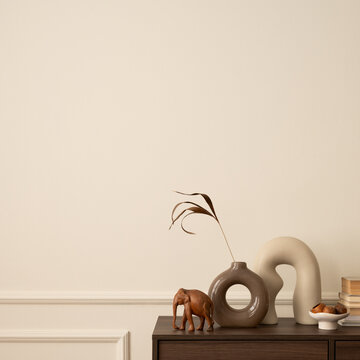 Minimalist composition of living room interior with copy space, wooden sideboard, vase with dried flowers, modern sculpture, books, beige wall with stucco and personal accessories. Home decor Template