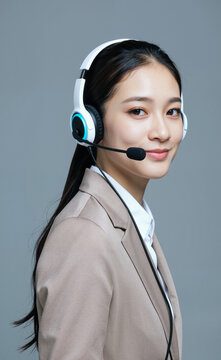 年轻亚洲女性在客服或呼叫中心工作时戴着耳机微微微笑的肖像，耳机麦克风靠近嘴边，背景简洁