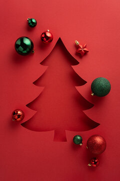 红色垂直背景上有一个风格化的圣诞树剪纸，周围环绕着绿色和红色的装饰球，营造出适合贺卡和季节性项目的节日氛围场景