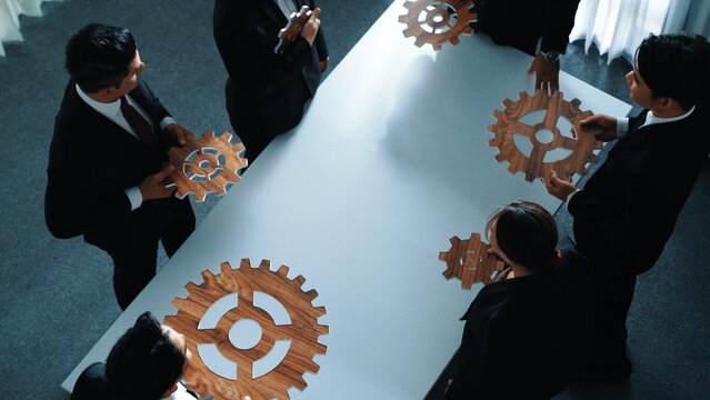 在会议上，专业商务人士分离木制齿轮的俯视图。一群项目经理在会议室或工作场所互相协助、团队合作并寻找问题。象征着团结。董事会层面。