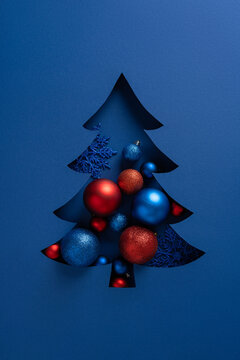 A vertical stylized blue Christmas tree cutout with red and blue ornaments creates a festive holiday card design suitable for Christmas and New Year greetings. Modern, bold, and decorative