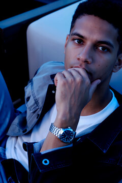 年轻黑人男子的肖像，坐着，手托下巴，若有所思地望着镜头，戴着手表，能看到短卷发。