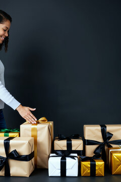 年轻的黑人女性在纯色深色背景下整理多个系着丝带的包装礼盒时面带微笑，仅可见上半身和手部，右侧有文案空间