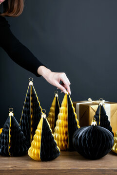 一位高加索年轻成年女性在木桌上摆放黑金纸制圣诞树，旁边有包装好的礼盒，仅露出手和部分手臂，呈现节日装饰场景