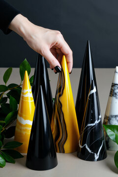 一位高加索年轻成年女性的手在绿叶间摆放有光泽的大理石纹装饰锥体，在中性背景上展示现代几何装饰物件