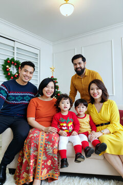 假日期间，多族裔的年轻男女与两个孩子坐在装饰有圣诞花环和圣诞树的客厅沙发上摆姿势对着镜头微笑