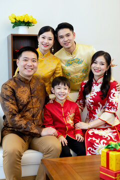亚洲家庭合影，两名年轻男子、两名年轻女子和一名小男孩身着传统服饰，在室内节日庆典中微笑着摆姿势