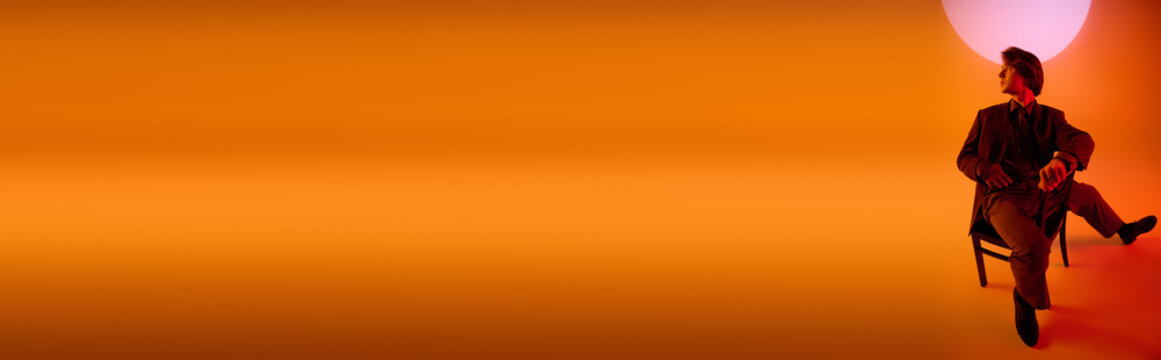 翻译标题：时尚青年倚着绚丽的落日背景坐在椅子上