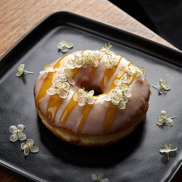 美食家级接骨木花糖霜甜甜圈，搭配可食用花朵置于黑色盘子上