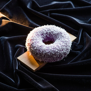 顶部撒有椰片的紫色紫山药甜甜圈，置于丝绒与木质展示架上