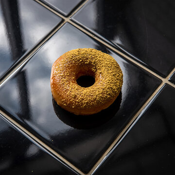 黑色光泽瓷砖表面带有反光的橙香香料甜甜圈