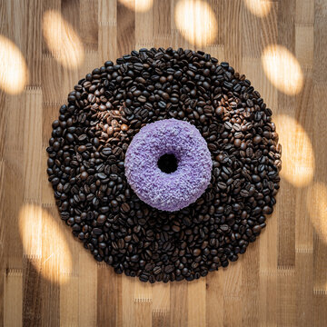 紫色甜甜圈置于深烘咖啡豆与木材图案中央