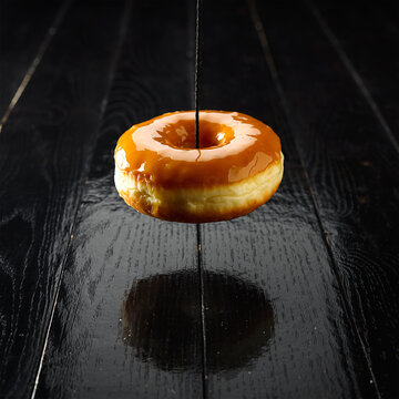 焦糖淋面甜甜圈悬浮在反光深色木质桌面上方