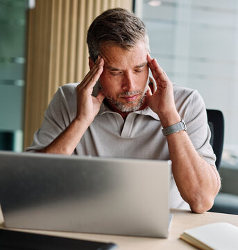 一位年轻商人、年轻企业家或学生在办公室使用平板或笔记本电脑工作时头疼、承受压力与紧张的肖像