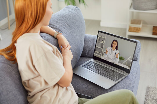 生病的年轻女孩在家使用笔记本电脑听取建议、预约并与一位友善的女医生进行在线视频通话。远程医疗与在线患者咨询概念