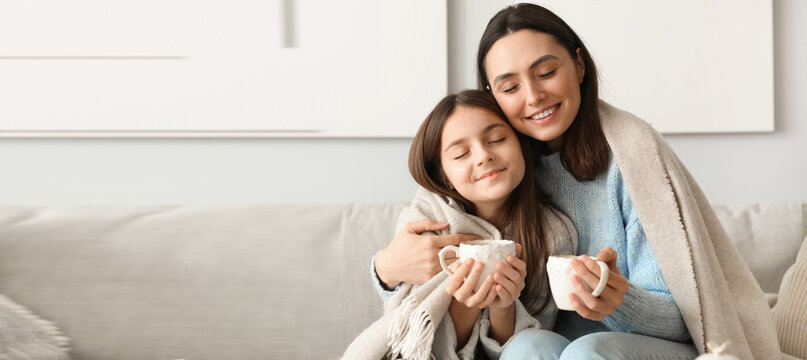 Little girl and her mother with cups of tea sitting at home
