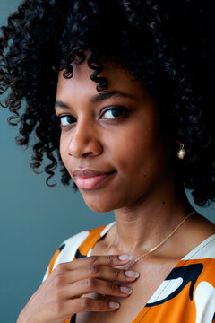 年轻成年黑人女性肖像：直视镜头，略带微笑，手触项链，展现自然卷发，佩戴简约首饰，背景纯色