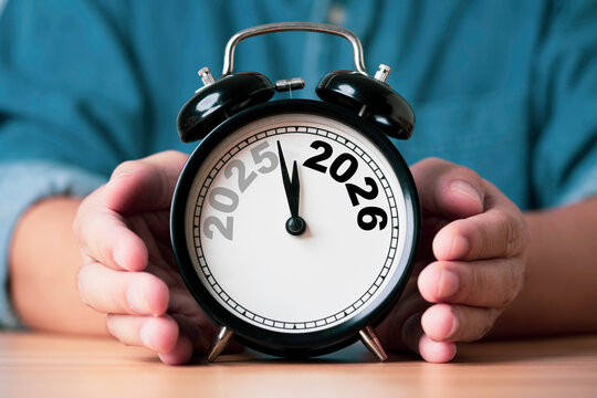 商人手持显示从2025到2026过渡的闹钟，象征着时间变化、新年规划、未来目标、战略以及为商业和个人发展所做的准备