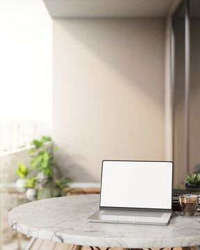 阳台上阳光照耀下的圆形大理石桌上放着咖啡杯和植物的黑屏笔记本电脑场景