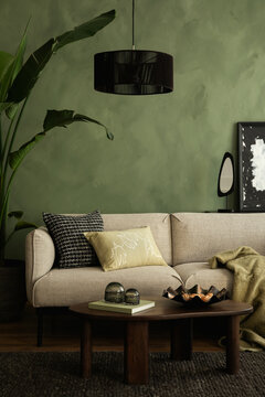 Modern living room with a beige sofa, green textured wall, black pendant lamp, and wooden coffee table with stylish decor.