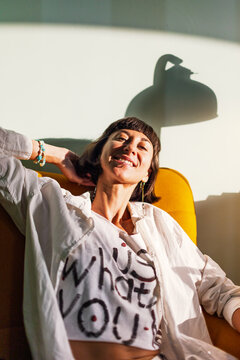 Beautiful woman sitting on yellow chair. Brunette with bob hair smiling at camera. Relaxed lifestyle concept.