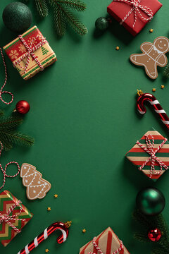 Festive vertical scene with wrapped gifts, candy canes, gingerbread cookies, and pine branches on a green backdrop