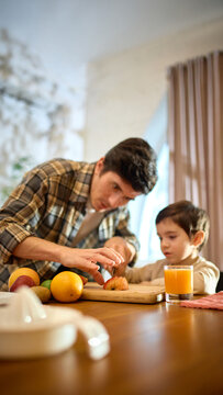 Orange juice glass in bright kitchen scene with lively warm father and little boy moment. Concept of lifestyle storytelling, health visuals, food promotion and positive emotional branding.