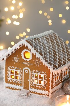 Beautiful gingerbread house and Christmas decor on table against blurred lights, closeup. Bokeh effect
