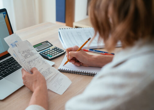 女子在家核对纸质账单并计算开支，肩后视角可见铅笔与计算器——家庭预算、明智理财及个人财务规划主题