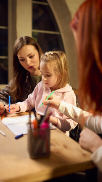 Woman guiding little girl during creative drawing session as second woman observes. Concept of shared learning, emotional support, inclusive family values, and nurturing home environment.