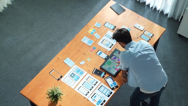 俯视图下，熟练商人在平板上查看UX UI设计，同时设计协议或选择线框图界面；聪明的白人前端开发者规划UI设计；集会场景