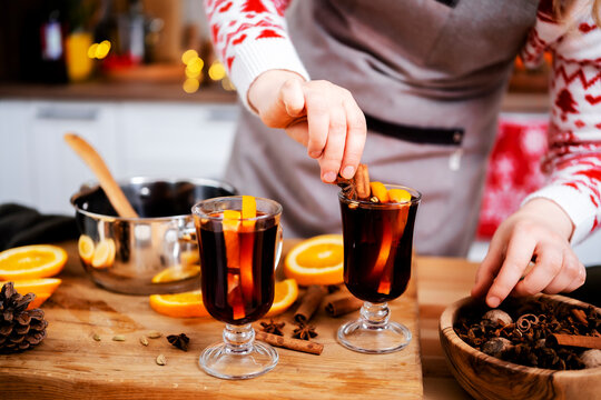 Woman garnishing hot mulled wine with cinnamon and star anise in christmas and new year kitchen creating warm aromatic holiday beverage with citrus and spicy winter notes