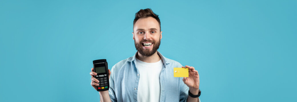 一位留着胡子的年轻男子一手开心地拿着支付终端，另一手拿着信用卡，站在明亮的蓝色背景前，展示数字支付的便捷性。
