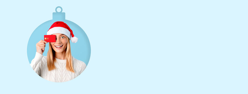 A cheerful woman wearing a Santa hat holds a gift card while smiling brightly against a light blue background. Her joyful expression captures the spirit of the holiday season.