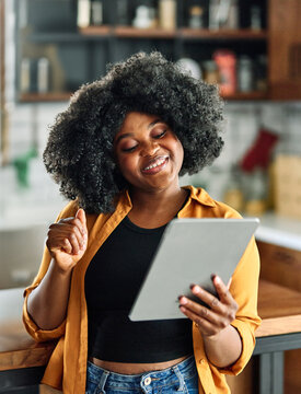 Happy young afro american woman having fun preparing food and looking for recipes online using a tablet in kitchen, or a young businesswoman working from home office making connections online